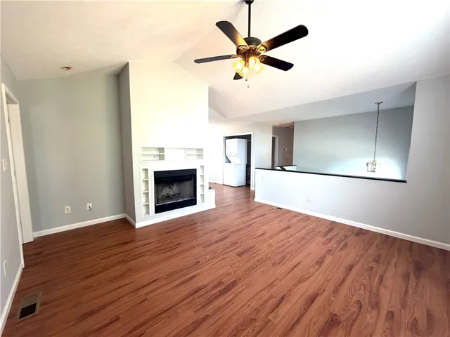 This inviting living space features vaulted ceilings, a cozy fireplace with built-in shelving, and warm wood flooring.