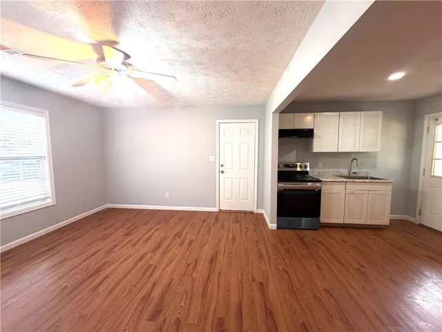 This versatile open-concept space features warm wood flooring, a kitchen area, and a ceiling fan for comfort.