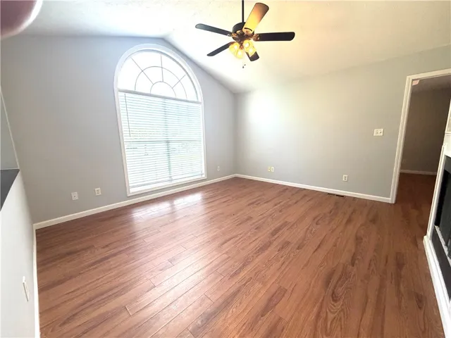 A spacious living area features a grand arched window and lustrous wood flooring.