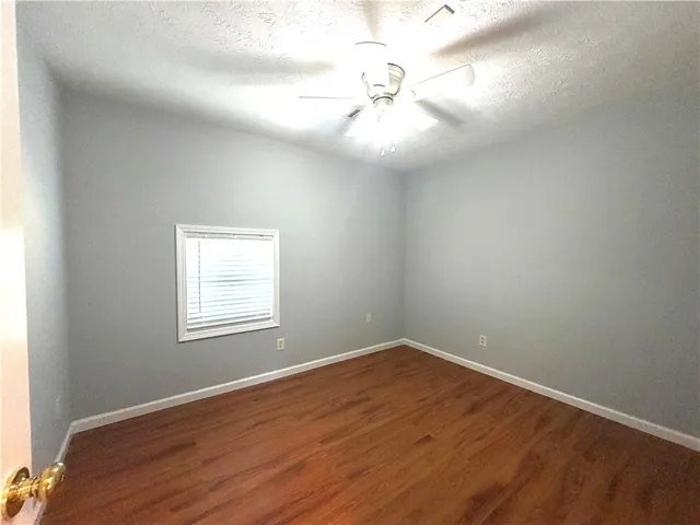 A well-proportioned bedroom with rich wood flooring and a convenient ceiling fan.