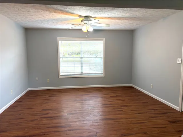 This naturally illuminated living area showcases rich wood flooring and a refreshing ceiling fan.