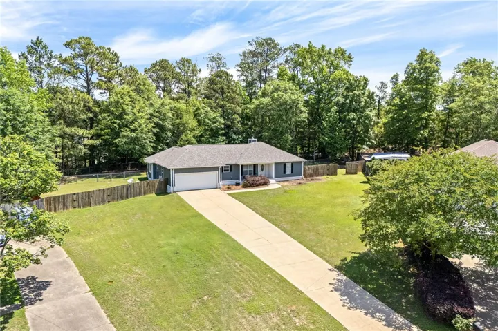 A well-maintained single-story residence with a long driveway, nestled amidst verdant landscaping and mature trees.