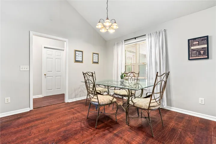 This dining area features rich wood flooring, a charming chandelier, and a sun-filled window with blinds.