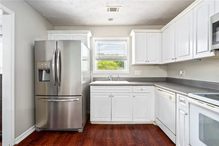 A well-equipped kitchen features dark wood floors, white cabinetry, and stainless steel appliances, creating a functional cooking space.