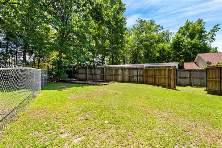 A spacious, fenced backyard offers ample green space and privacy with mature trees bordering the property.