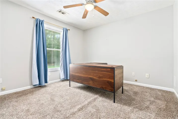 This naturally illuminated room features plush carpeting and a large window, creating a serene work-from-home environment.