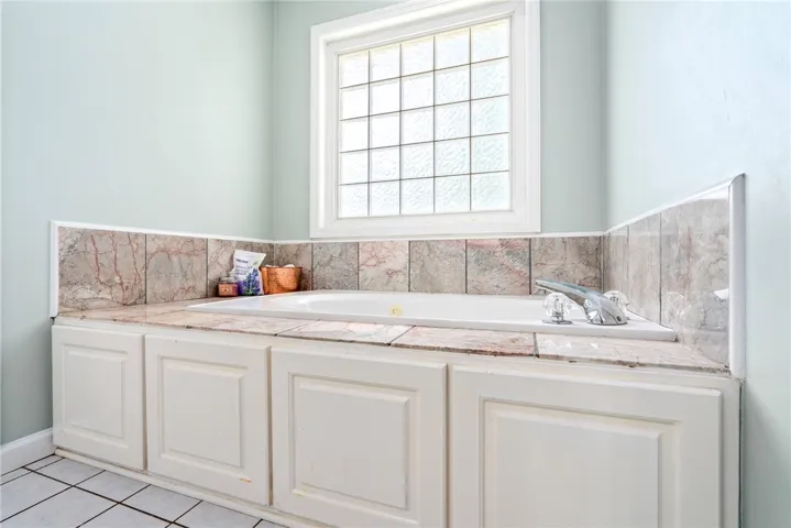 Relax and unwind in this inviting primary bathroom, featuring a built-in tub with elegant tile surround and a window for natural light.