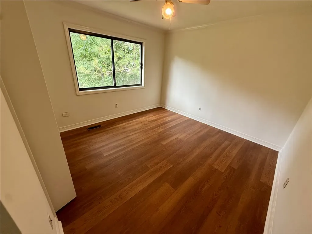 Rich hardwood flooring complements ample natural light in this serene and ready-to-personalize bedroom space.