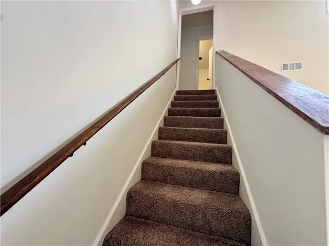 Ascend to comfort on this carpeted staircase, featuring rich wood handrails for a touch of elegance.