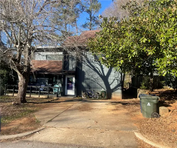 This residence features a welcoming facade with a covered deck and mature trees.