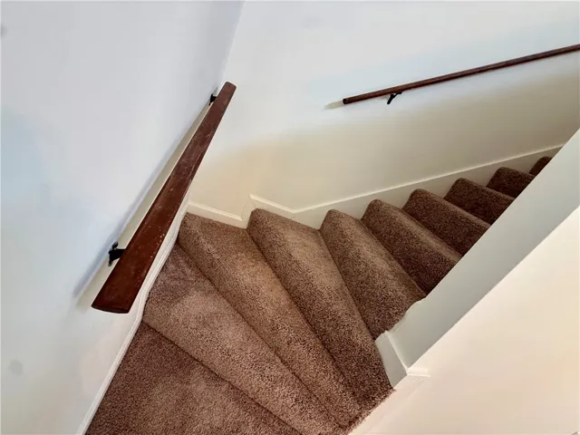 A descending staircase with plush carpeted treads and a sleek wooden handrail.