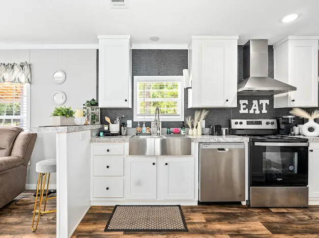 This modern kitchen features a spacious stainless steel sink and appliances, complemented by clean white cabinetry and dark wood-look flooring.