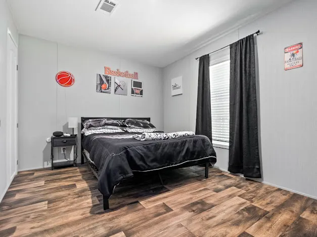 This naturally illuminated bedroom showcases rich wood flooring, offering a comfortable and inviting atmosphere.