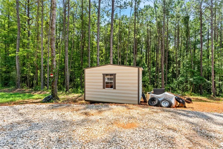 A well-maintained utility shed stands amidst a lush, wooded landscape with a gravel foreground.