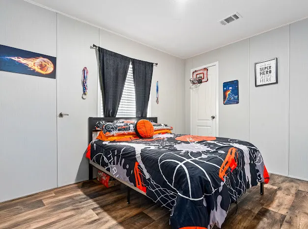 This cozy bedroom offers rich wood flooring and a window with blinds, creating a comfortable and inviting atmosphere.