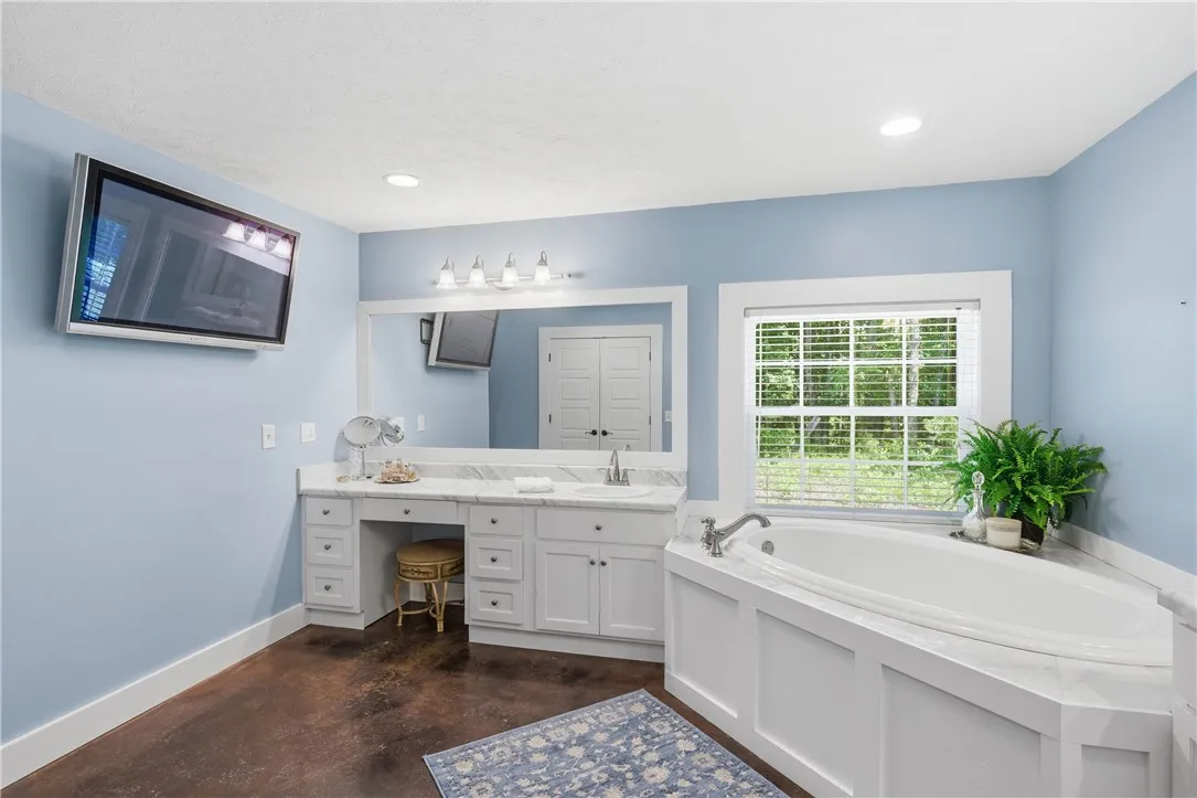 This primary bathroom features a corner soaking tub and a spacious vanity with a single sink and makeup area, all beneath recessed lighting.