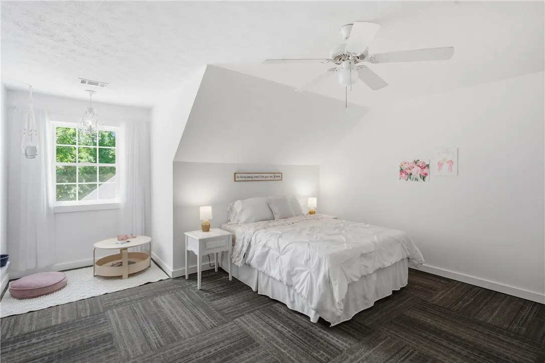 This peaceful bedroom retreat features soft gray flooring and a classic window offering lush outdoor views.