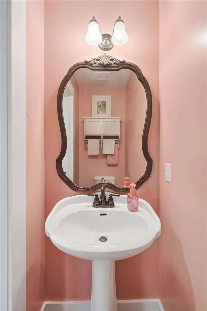 This powder room features a classic pedestal sink, an ornate framed mirror, and a wall-mounted light fixture.