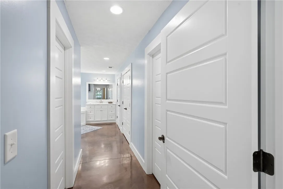 A well-lit hallway with white paneled doors leads to a bathroom featuring a large vanity and mirror.