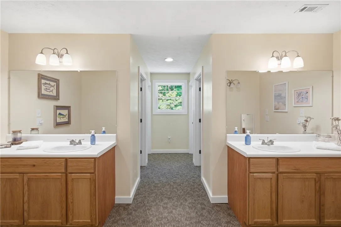 This functional bathroom features two separate vanities with expansive mirrors and a windowed hallway leading to additional private spaces.
