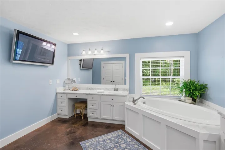 This primary bathroom features a corner soaking tub and a spacious vanity with a single sink and makeup area, all beneath recessed lighting.