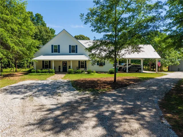 A classic white country home welcomes with blue shutters and a gravel driveway through mature trees.