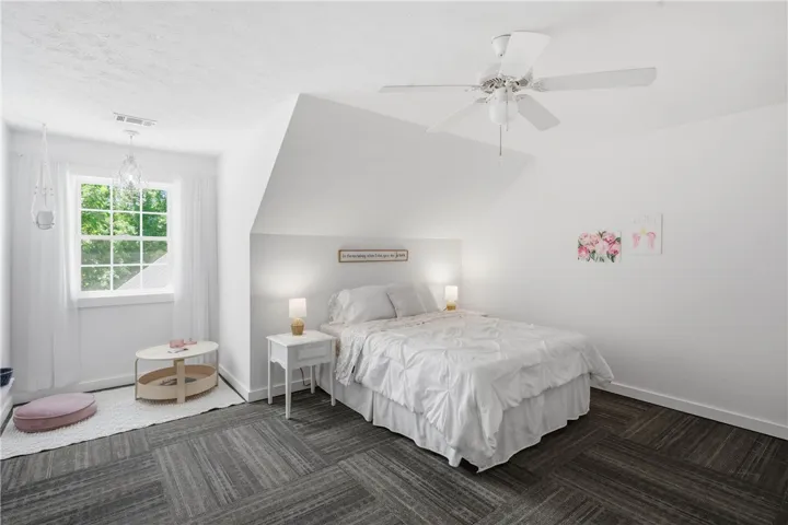 This peaceful bedroom retreat features soft gray flooring and a classic window offering lush outdoor views.