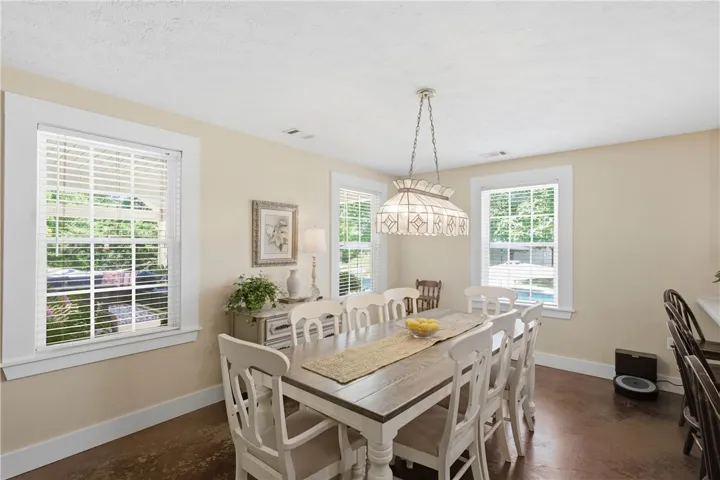 An inviting dining area offers a well-lit space for meals, featuring a central chandelier and ample natural light from multiple windows.