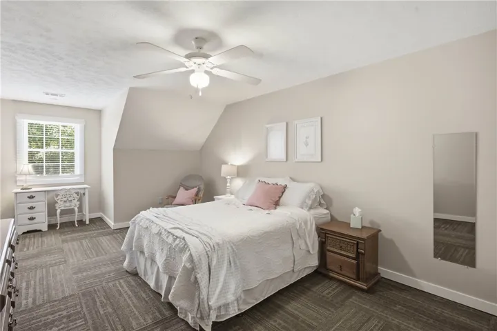 This naturally illuminated bedroom offers a cozy ambiance with a ceiling fan and patterned flooring.