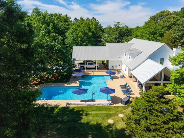 An aerial perspective reveals a serene home with an elongated pool, surrounded by mature trees.