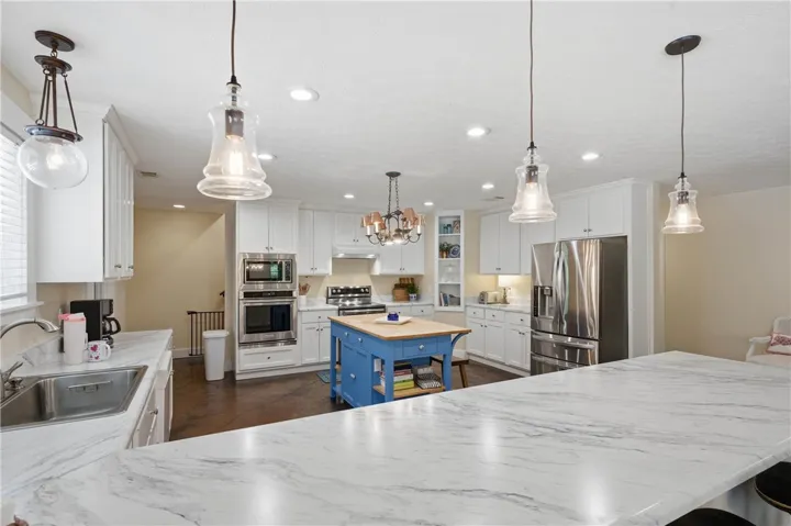 This kitchen showcases a functional layout with white cabinetry, stainless steel appliances, and a central blue island.