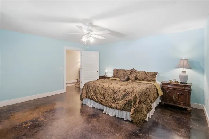 This spacious bedroom features unique, richly toned concrete flooring and a classic ceiling fan for comfort.