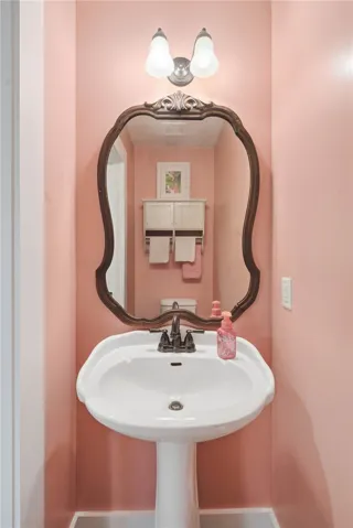 This powder room features a classic pedestal sink, an ornate framed mirror, and a wall-mounted light fixture.