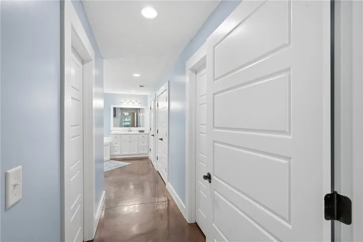 A well-lit hallway with white paneled doors leads to a bathroom featuring a large vanity and mirror.