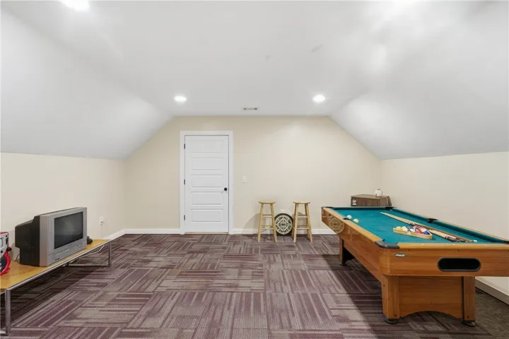 This versatile recreation room, with its sloped ceilings and recessed illumination, offers ample space for various activities.