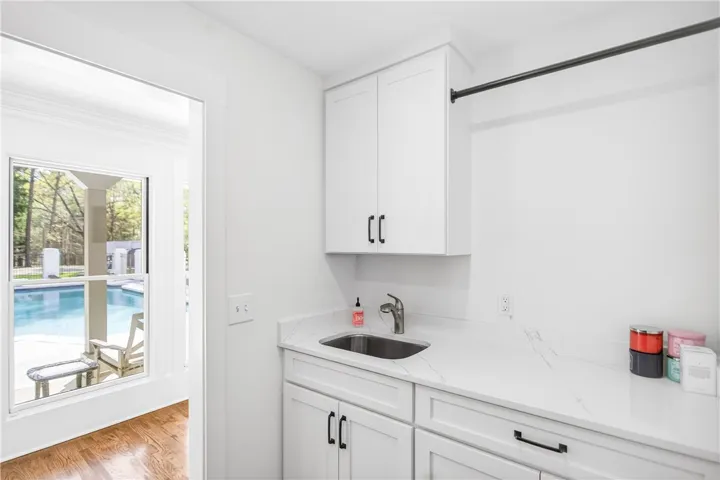 White cabinetry and stone counters define this practical laundry area, overlooking an inviting pool.