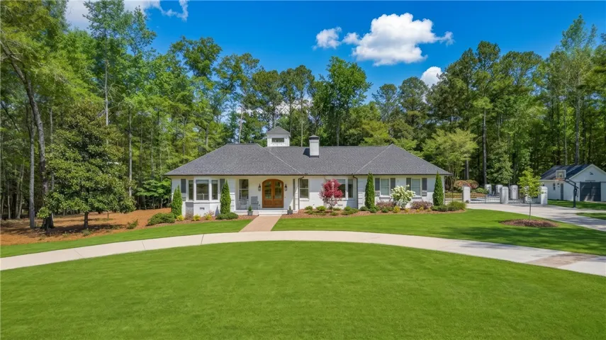 A graceful home sits on a sprawling lawn, framed by a classic dark roof and mature trees.