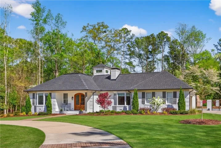 Elegant single-story home with a manicured lawn and a winding driveway, nestled amidst lush trees.