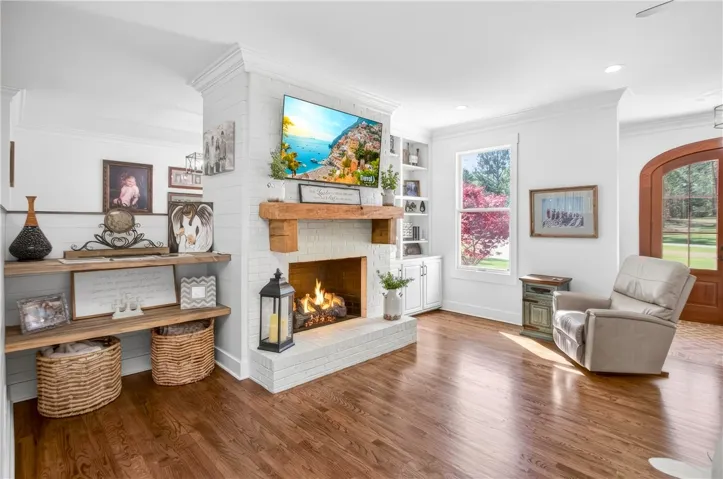 A comforting glow emanates from the hearth of a white brick fireplace, anchoring this inviting living space with warm hardwood flooring.