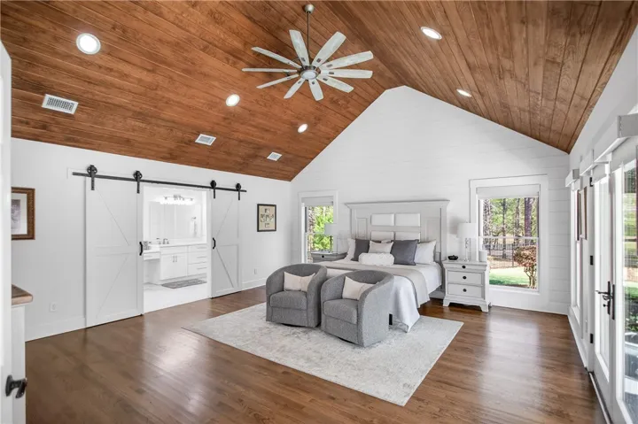 A spacious primary suite features soaring vaulted ceilings with natural wood, leading to a luxurious bathroom behind barn doors.