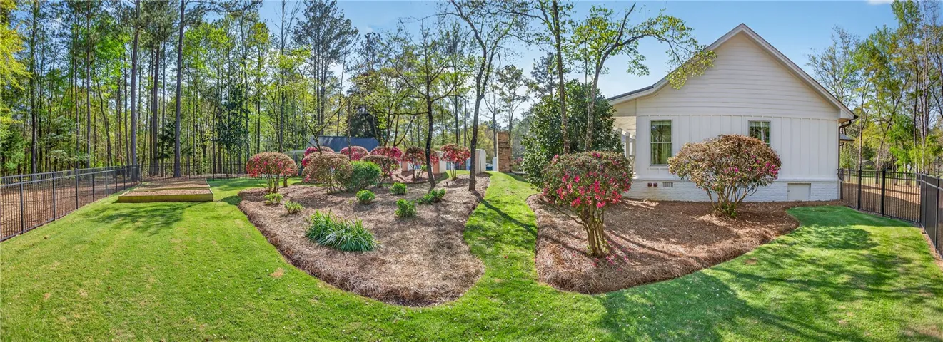 A fenced backyard retreat offers lush green lawn and vibrant landscaping, with mature trees bordering the property.