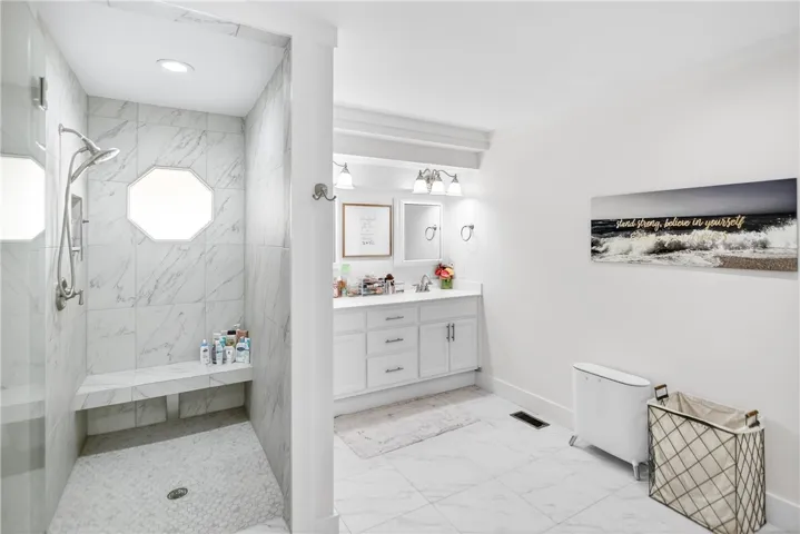 Marble-tiled shower with built-in bench complements the dual vanity, providing ample space for personal routines.