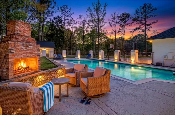 An inviting backyard oasis offers a sparkling in-ground pool alongside a cozy outdoor fireplace, perfect for evening relaxation.