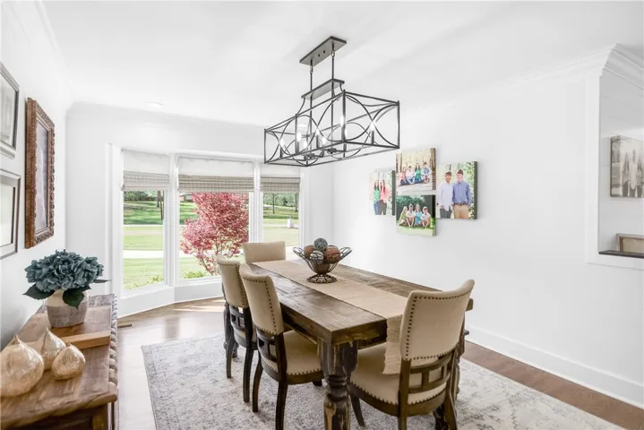 A refined dining space presents ample seating, an intricate chandelier, and verdant outdoor views.