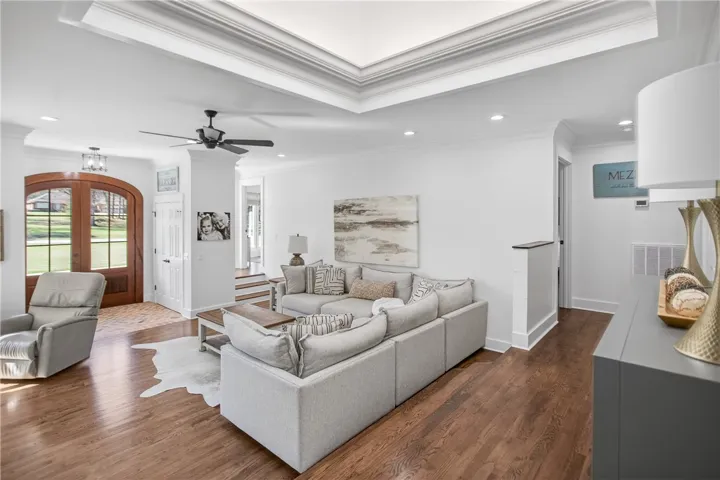 Hardwood flooring and crown molding accent this comfortable living area, featuring an impressive tray ceiling and elegant French doors.