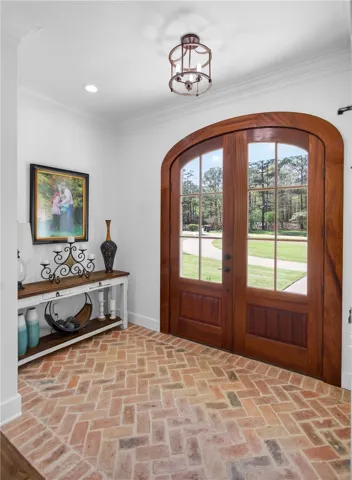 Arched double doors with glass panels invite natural light into this welcoming entry, featuring intricate brick flooring.