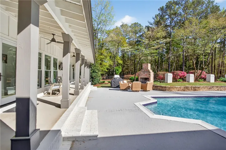 An inviting veranda overlooks a tranquil pool and a lush, tree-lined landscape.