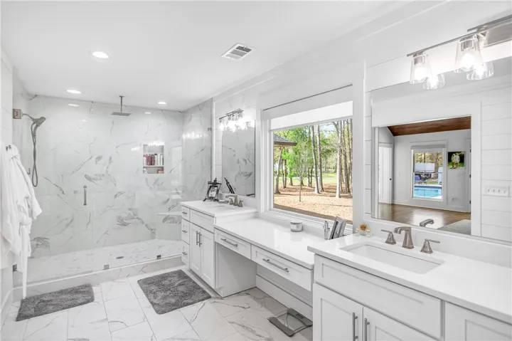 Marble-clad shower and dual vanities frame a bright window, offering a refreshing outdoor vista and a peek at the pool.