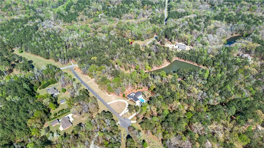 An aerial panorama reveals a vast, wooded property with several homes and a glistening pool nestled beside a tranquil lake.
