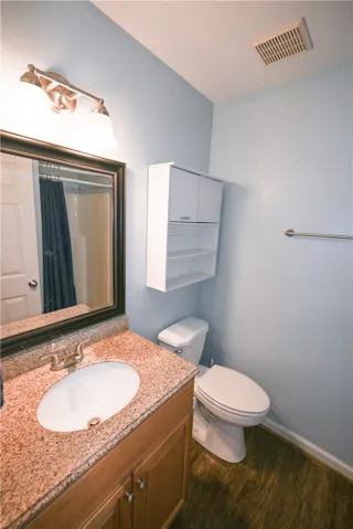 A compact bathroom featuring a vanity with granite counters, an oval sink, and a toilet, complemented by wood-look flooring.